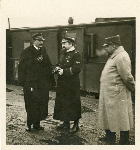 [Trois officiers, dont un commandant au centre, discutant devant un train]